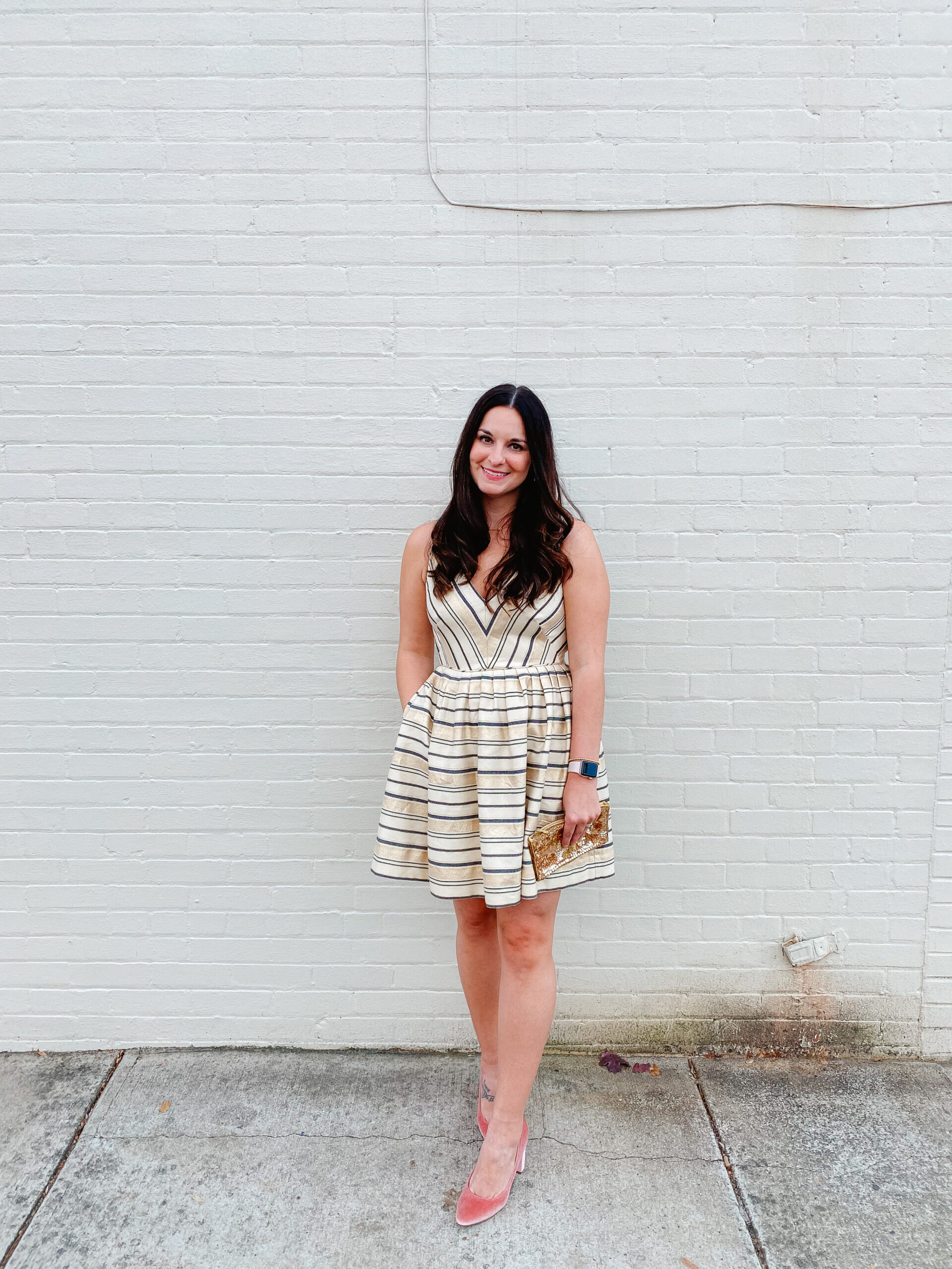 Emily Soto in a cream colored striped dress with a gold clutch purse 